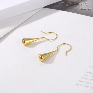 Macro shot of minimalist gold teardrop earrings on white card, showing polished metal texture