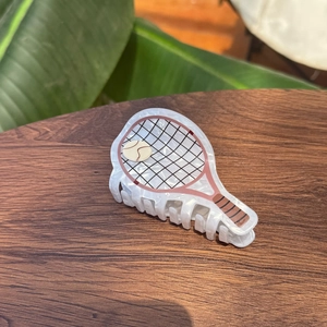 Détail de la pince à cheveux raquette de tennis en acétate blanc sur bois rustique