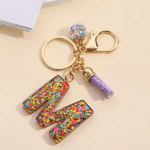 Detail of resin letter M keychain with colorful sequins, purple tassel, and golden hardware
