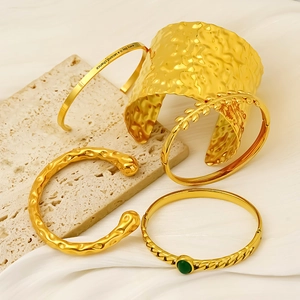 Gold plated stainless steel bracelets with textures and green gemstones on silk background