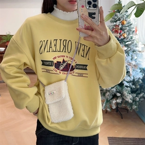 Close-up of white plush crossbody phone bag with purple lanyard on yellow sweatshirt