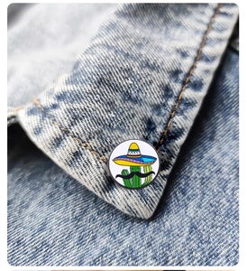 Close-up of a cartoon cactus enamel pin with sombreros on a denim jacket collar