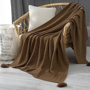 Close-up of brown waffle weave knit blanket with decorative pompoms on a rattan chair
