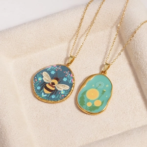 Vintage gold titanium necklaces with bee and dandelion glass gems on beige tray