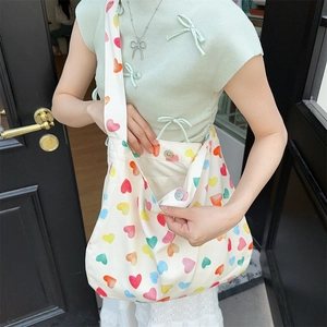 Close-up of off-white canvas shoulder bag with heart prints and magnetic buckle detail