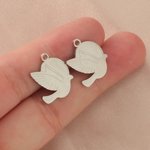 Polished mirror stainless steel peace dove bird charm pendants shown on a fingertip