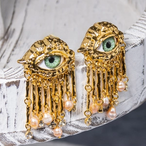 Detail of gold evil eye earrings featuring green iris, long tassels and pink pearls