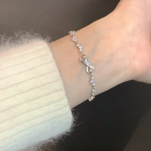 Detail of silver bow bracelet with zircon stones worn by a model on a plush background