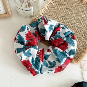 Detailed view of a soft fabric scrunchie with red rose and leaf print on white background