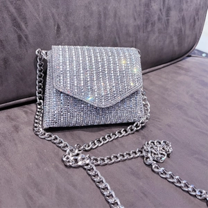 Detail of silver rhinestone evening bag with thick metallic chain on textured background