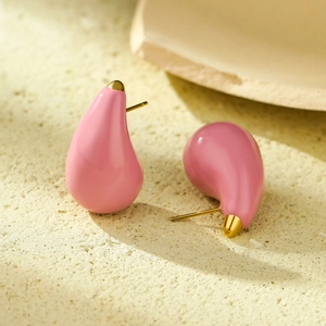 Detail of pink enamel teardrop earrings with elegant golden metal caps on sandy surface