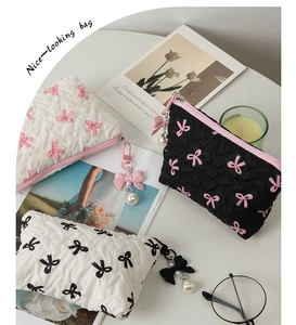 Three quilted cosmetic pouches with bows and pearl zipper charms on a white desk