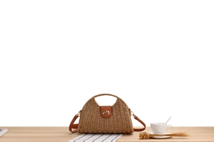 Detailed close-up of khaki woven straw bag with brown leather strap and gold hardware on wood
