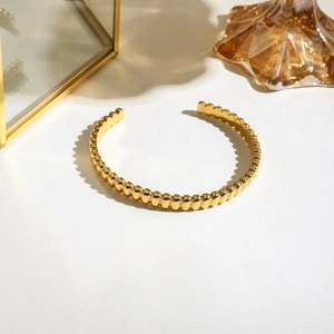 Détail d'un bracelet ouvert à billes dorées sur fond blanc avec verre ambré