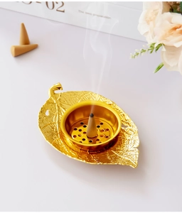 Detailed view of leaf-shaped gold incense burner with burning incense cone and smoke