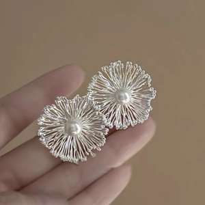 Close-up of a silver petal earring with a central pearl held against a warm beige background