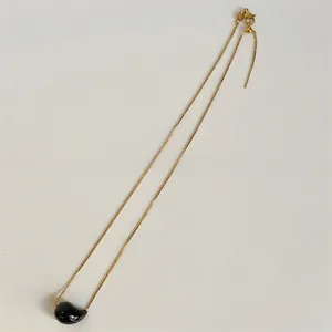 Detailed view of the gold chain necklace featuring a glossy black teardrop pendant