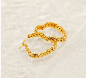 Close-up of golden wheat ear heart earrings with braided texture and snap closure detail