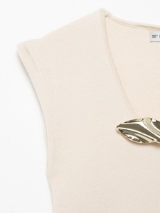 Detail of light beige knit top featuring golden leaf metal buckle and soft fabric texture