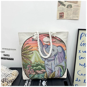 Detailed embroidery of elephant and landscape on a woven beige tote bag with rope handles