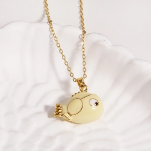 Close-up of a gold chain necklace with a cute yellow cartoon fish pendant on a shell tray