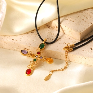 Gold cross necklace with colorful stones and pearls on a black cord over beige silk