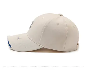 Close-up of beige cotton baseball cap featuring distressed brim and side letter patch