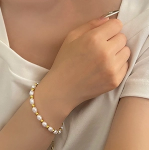 Detailed shot of white oval pearls and gold beads on a delicate bracelet worn on wrist