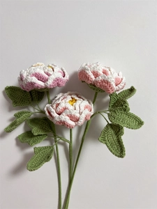 Detailed close-up of three handcrafted pink and white crochet peony flowers with green leaves