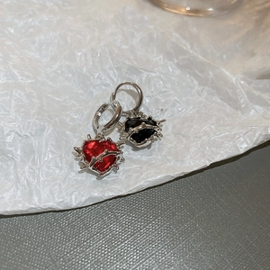 Detail of thorn heart drop earrings in red and black on textured white background