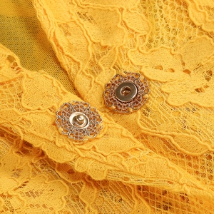Dettaglio macro del pizzo giallo e della fibbia in metallo dorato a forma di fiore sulla tuta