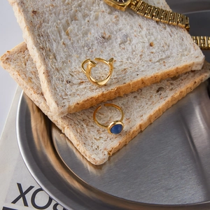 Detail of gold nail style open ring and blue stone ring on a stainless steel tray