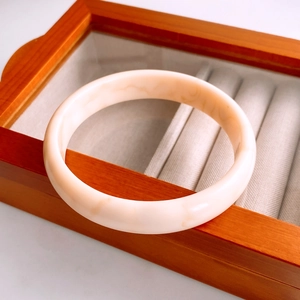 Gros plan d'un bracelet en résine beige marbré posé sur un coffret à bijoux en bois vintage