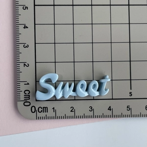 Macro d'une breloque Sweet en résine bleu clair sur tapis de coupe mesurant 4cm