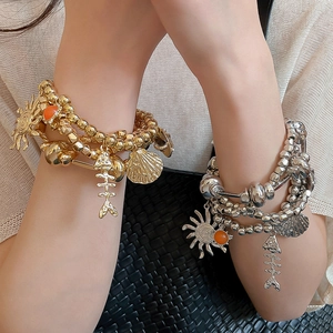 Detail of layered beaded bracelets with metallic charms such as fishbone and sun on wrist
