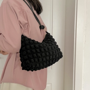 Vista dettagliata della borsa a spalla nera con trama a bolle indossata da una modella
