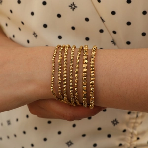 Detail of layered gold beaded bracelet featuring faceted beads and metallic cubes