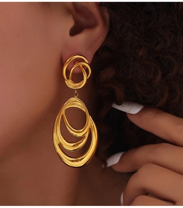 Close-up of layered golden oval hoop earrings on model showing textured metallic finish