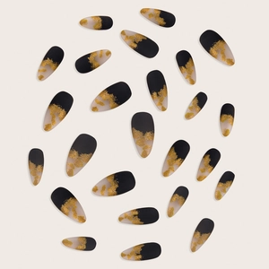 Flat lay of long almond press-on nails with black gradient and gold foil flakes design