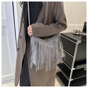 Detail view of a light gray bucket bag with long fringe tassels on a stylish model