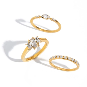 Three gold titanium steel rings with round and rectangular clear crystals on white background