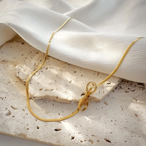Detailed close-up of golden bow pendant with snake chain on elegant textured background