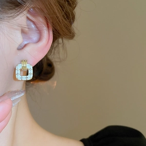 Close-up of golden square stud earring with white enamel pattern and tiny diamonds