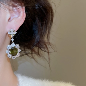 Close-up of olive green flower earrings with white zircon on a model's ear