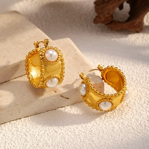 Vintage gold hoop earrings with white pearls and beaded edges on stone background