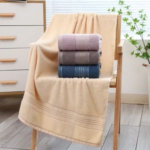 Thick soft cotton bath towels in beige and purple stacked on a wooden chair