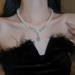 Close-up of pearl necklace with a teardrop diamond pendant worn by a model in soft light