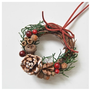 Detail of mini Christmas wreath with pine cones, red berries and suede ribbon on rattan base
