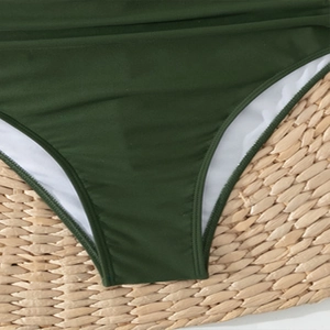 Detailed close-up of dark green swimsuit fabric with premium white lining on straw mat