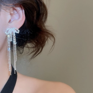 Close-up of elegant silver bow earrings with sparkling rhinestone tassels worn by a model